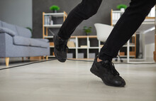 Person In Uncomfortable Sneakers Trips Over Electric Cord At Home. Closeup Male Office Worker In Black Shoes Stumbles On Power Cable. Close Up Shot Feet Stepping On Floor. Injury And Accident Concept