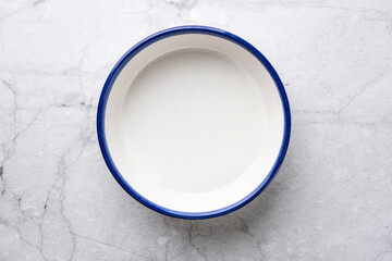 Empty white ceramic plate with blue rim on white marble table background