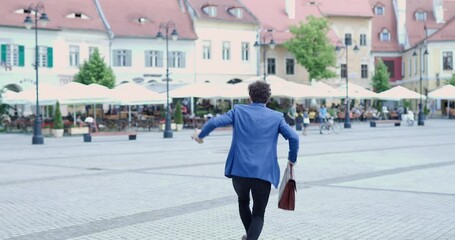 Poster - enthusiastic man in smart casual outfit with suitcase having fun and dancing in medieval town in Romania