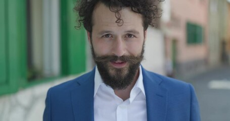 Sticker - close up of charming curly hair guy smiling and being happy, looking to side and making a shocked face on a old city background