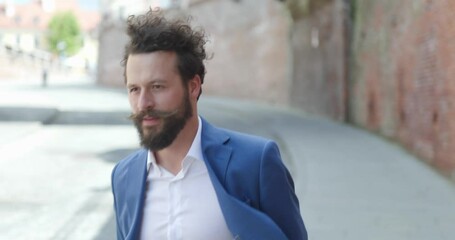 Poster - sexy unshaved man wearing blue jacket, holding suitcase and confidently walking in a medieval city from Romania