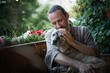 handsome bearded gentle middle-aged man hugging his dog while sitting on an open terrace at home during sunset