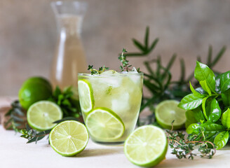 Cold refreshing summer drink or lemonade with lime and thyme on concrete background.