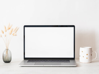 Home office desk with open laptop, dry autumn branches in vase and white mug