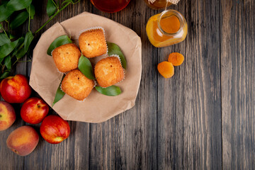 Poster - top view of muffins with green leaves on craft brown paper with fresh ripe nectarines and peach jam in a glass jar on rustic wooden background with copy space