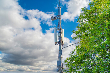 A cell tower against the background of a calm sky with clouds. Transmitters with 5G telephone communication system antennas.