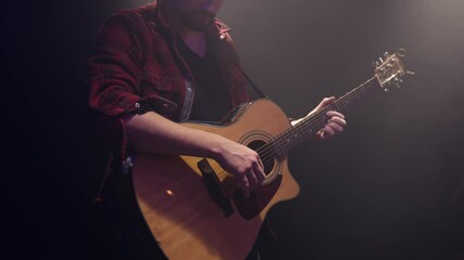 Wall Mural - A male guitarist plays chords on an acoustic guitar in a dark room.