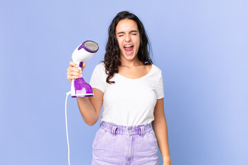 Wall Mural - hispanic pretty woman shouting aggressively, looking very angry and holding an iron steam