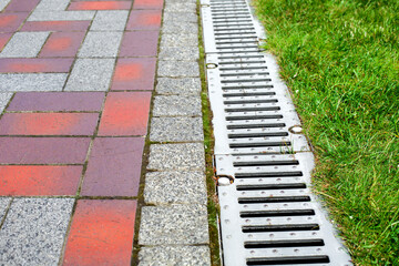 Wall Mural - grating of the drainage system for drainage of rainwater in the park at the edge of the sidewalk from a stone slab with a green lawn, landscaping a city garden close-up, nobody.