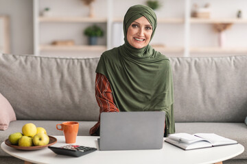 Wall Mural - Happy Mature Islamic Lady Using Laptop Smiling Sitting At Home