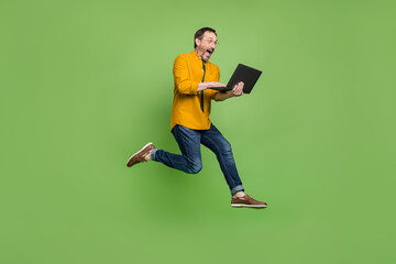 full size photo of brown haired happy amazed man jump up run hold laptop isolated on green color bac