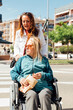 © ADDICTIVE STOCK - Aged mother in wheelchair and adult daughter walking in city