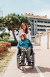 © ADDICTIVE STOCK - Aged mother in wheelchair and adult daughter walking in city