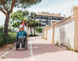© ADDICTIVE STOCK - Aged mother in wheelchair and adult daughter walking in city