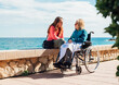 © ADDICTIVE STOCK - Daughter and senior mother in wheelchair on promenade