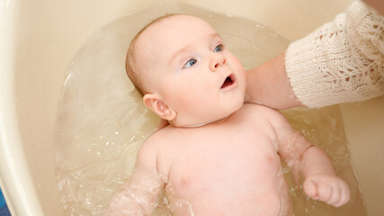 Wall Mural - Closeup of mother supporting baby head while washing in bath. Concept of parenting ,baby care and healthcare