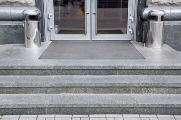 granite gray threshold steps with a foot mat at the entrance to the front door made of tempered glass architecture market style with trash can near facade, nobody.