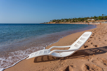 White plastic sun lounger near sea water on a tropical beach in Sharm El Sheikh, Egypt