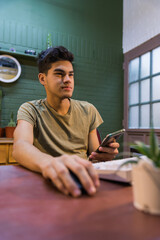 teenage boy sitting at home desk, using cell phone and computer