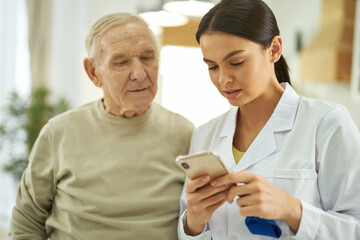 Wall Mural - Nurse and senior citizen looking at mobile phone screen