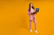 © alfa27 - pretty elegant foxy ginger redhaired lady walking carrying laptop isolated on bright yellow orange studio background, copy space. caucasian woman working on laptop, freelance