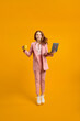 © alfa27 - Full length profile photo of funny business lady jump high up hold laptop and cup of coffee in hands addicted worker always online wear pink suit outfit, white sneakers, isolated yellow background