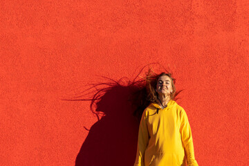 Portrait of a young woman in yellow hoodie on a red wall background. Outdoor photo, close-up.