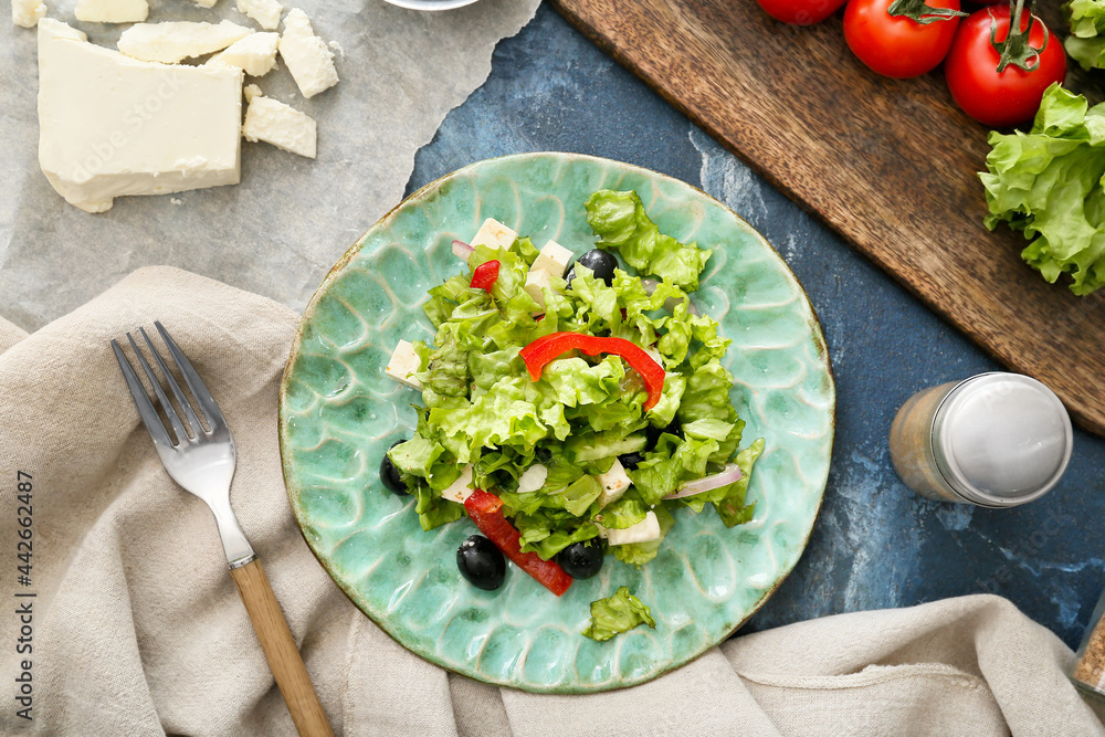 Plate with fresh Greek salad and ingredients on color background