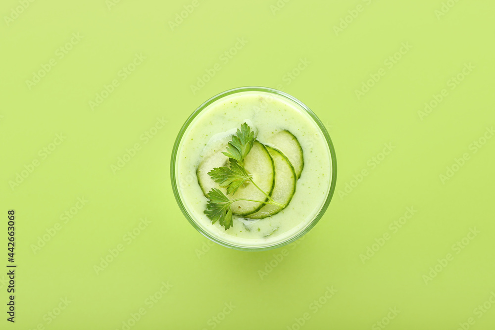 Glass with green gazpacho on color background