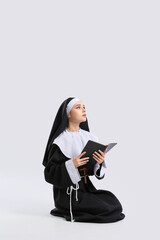 Wall Mural - Young praying nun with Bible on light background