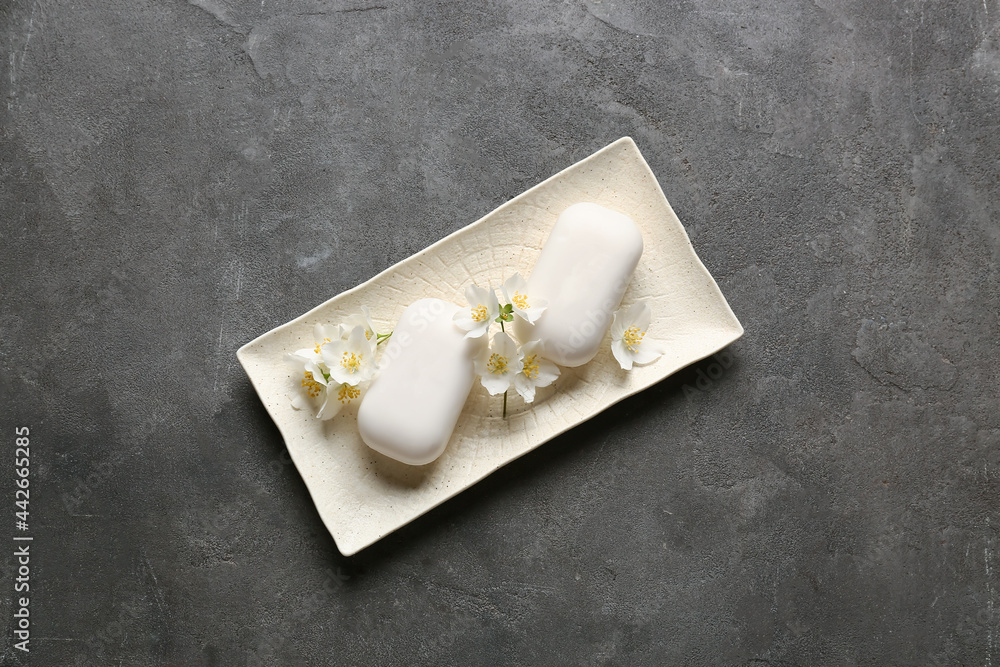 Plate with soap bars and flowers on dark background