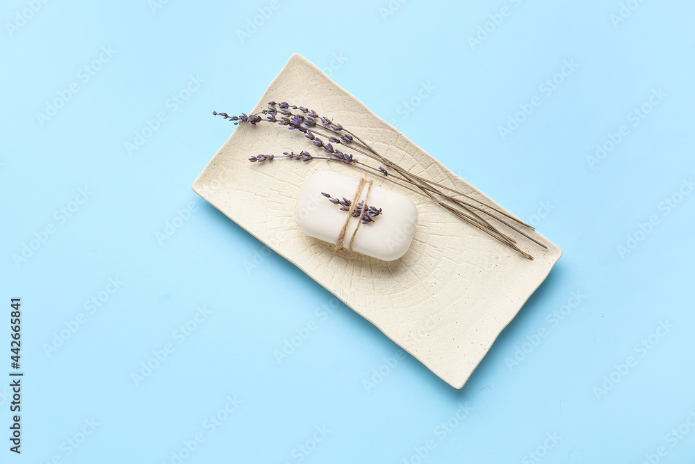 Plate with soap bar and flowers on color background