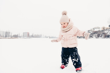 Canvas Print - Happy laughing girl wearing a pink jacket, scarf and hat, playing in a beautiful snowy winter walk. Girl enjoys winter, frosty day. Playing with snow on winter holidays. Winter holidays concept.