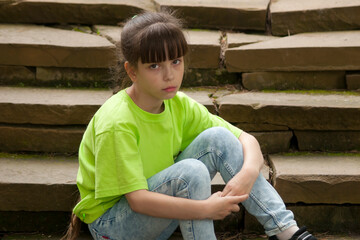 Sad child. The sad little girl (eight years old) sits on the old steps. Looking into the camera. One person. Outdoors