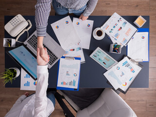 Top view of business women shaking hands in corporate office, sitting at desk, working in corporate bulding. Celebrating success of contract agreement negotation.