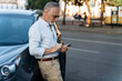 Middle aged man standing near his SUV car and using his smartphone. Portrait of senior man outdoors.