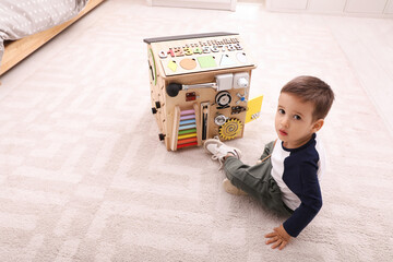 Wall Mural - Little boy playing with busy board on floor at home