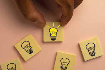 Hand choosing light bulb with glowing one different idea on wooden cube block over pink pastel background use for Creative idea and innovation,uniqueness,Education concept.