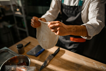 focus on male hands who prepares the dough for the pizza base