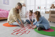 © New Africa - Mother and little girls taping sticker hopscotch on floor at home