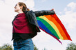 © ADDICTIVE STOCK - Cheerful woman with waving rainbow flag in city