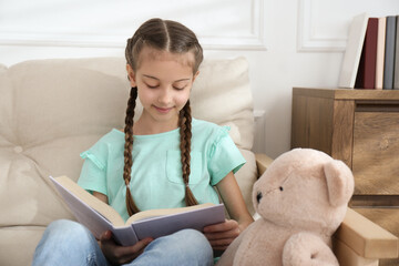 Wall Mural - Cute little girl reading book on sofa at home