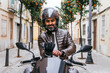 © ADDICTIVE STOCK - Smiling ethnic motorcyclist putting on glove on bike in town