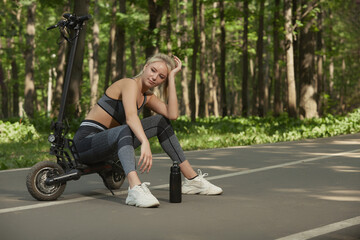 The girl rests in the park sitting on an electric scooter, there is a free place for advertising. Environmental mode of transport.