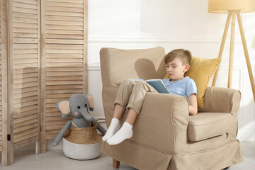 Wall Mural - Little boy reading book in armchair at home