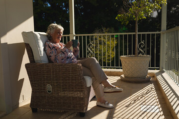 Wall Mural - Senior caucasian woman sitting on balcony holding mug and smiling