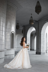 Wall Mural - A beautiful bride wearing a luxurious lace bridal dress posing outdoors. Outdoor romantic portrait of attractive brunette woman with bright makeup and wedding hairstyle