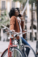 Cheerful Black Woman Talking On Smartphone Near Bicycle
