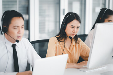 Team of call center staff in Asia wearing headphones with microphones. Stress and headaches while serving customers at desks and computers. Service concept and consulting. communication concept.