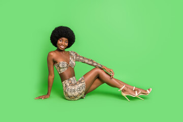 Sticker - Full length photo of sexy shiny dark skin lady wear print costume sitting floor smiling isolated green color background